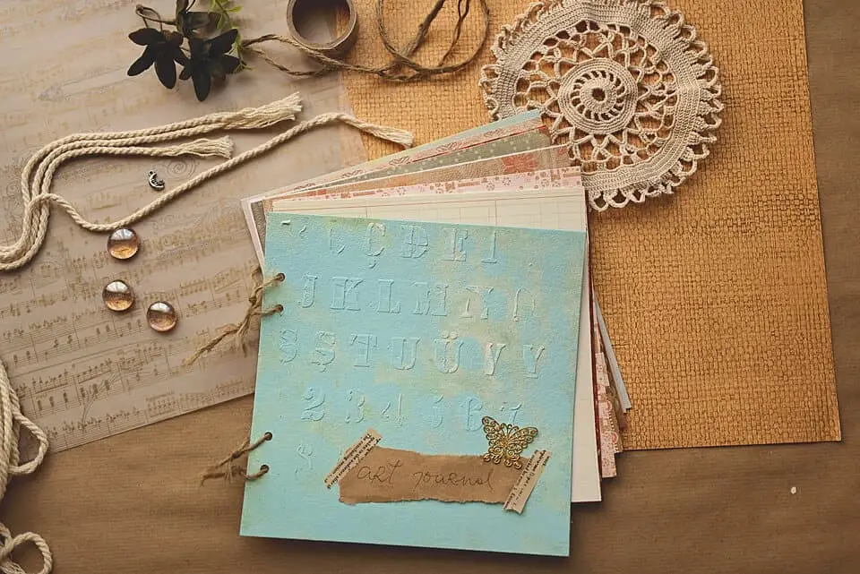 A photo of a DIY art journal on a brown aper. the journal is light blue and bound with a twine