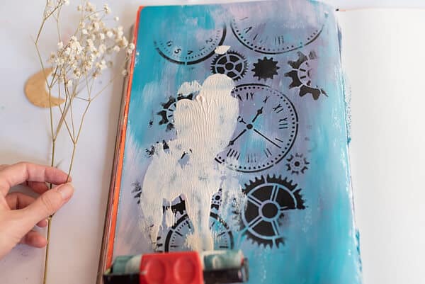 applying white paint with a brayer in an art journal