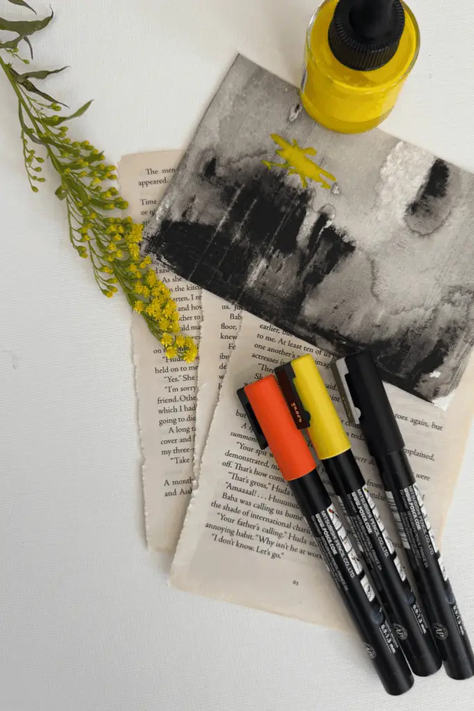 Basic art journal supplies for beginners including paint markers, collage paper, and acrylic ink.